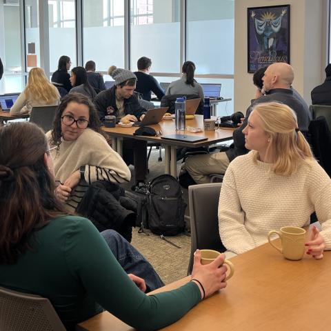 Students gather around different tables doing work and talking