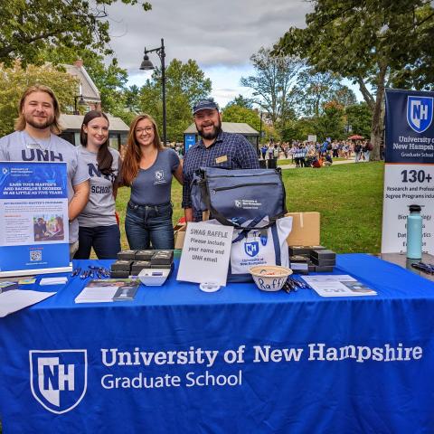 A group of college representatives stand behind a table full of promotional materials.
